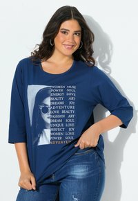 Granatowa bawełniana koszulka z rękawami do trzech czwartych, z graficznym nadrukiem przedstawiającym kobietę w okularach przeciwsłonecznych oraz inspirującym tekstem w różnych czcionkach.