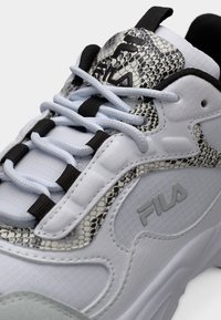 Λευκό αθλητικό παπούτσι FILA με ανοιχτό μπλε κορδόνια, μαύρες πινελιές και λεπτομέρειες με σχέδιο φίδι στη γλώσσα και τις πλευρές.