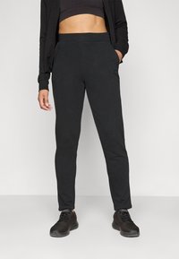 Sorte joggebukser med en glatt tekstur, elastisk midje og sidelommer, sammen med sorte joggesko. Enkel, strømlinjeformet design.