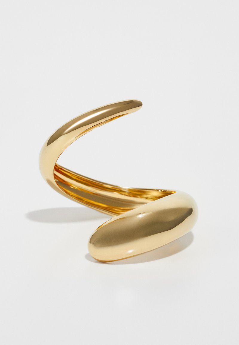 Gold metallic bracelet with a fluid, twisting design. Smooth, polished surface with a reflective finish and a tapered end.