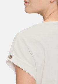 Witte top met korte mouwen en opgerolde mouwen, met een knoopaccent in een luipaardprint. Zachte stof met een gladde textuur.