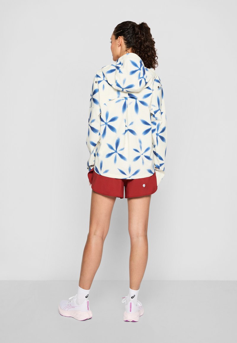 Hoodie aus Fleece mit weißem Grund und blauem Blumenmuster, kombiniert mit roten Shorts. Verfügt über lange Ärmel und eine lässige Passform.