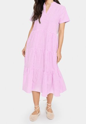 Vrouw die een midi-jurk draagt met verticale roze en witte strepen, korte mouwen en een V-hals, gecombineerd met beige veterschoenen met platte zool.