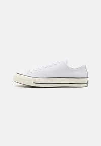 Valged lõhikuga kanva sneakerid lamepaeltega, mustade kummitaldadega ja kontrastse musta triibuga keskmisel taldal. Tekstureeritud pind.