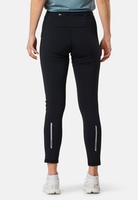 Leggings sportivi neri con una vestibilità slim, dotati di una tasca con zip sul retro e dettagli riflettenti vicino alle caviglie. Tessuto liscio e elasticizzato.