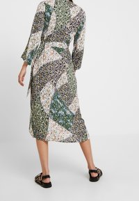 Vestido midi de múltiples patrones con diseños florales y geométricos en verde, blanco y azul marino. Presenta mangas tres cuartos y un cinturón atado.