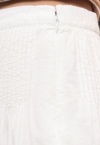 Κοντινή λήψη στη μέση λευκού ενδύματος με ορατό κλείσιμο φερμουάρ και υφασμάτινες ραμμένες λεπτομέρειες με υφή.