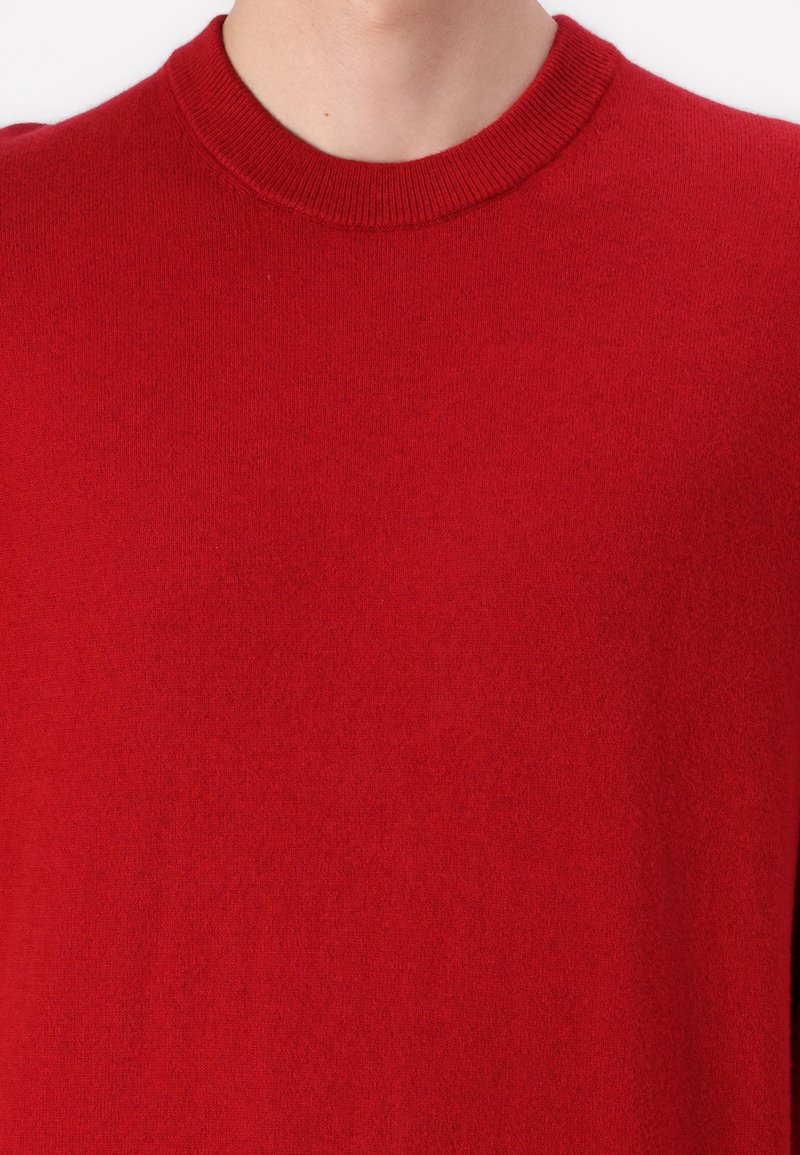 Suéter de punto rojo con cuello redondo acanalado y una textura suave. La tela parece ligera y el ajuste es casual.