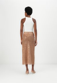 Bela rebrasta majica na bretelje uparena s dugom, sjajnom, prozirnom suknjom od bakrenih šljokica koja otkriva noge. Jednostavne sandale upotpunjuju odijelo.