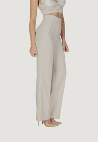 Pantaloni beige a vita alta con un design strutturato, texture liscia e chiusura con bottone frontale. Abbinati a tacchi a punta in tonalità neutra.