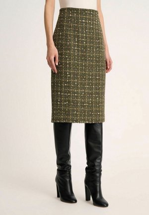 Grøn tweed blyantskirt med en struktureret silhuet, der har en tekstureret vævning og subtile flerfarvede prikker. Kombineret med sorte læder lårhøje støvler.