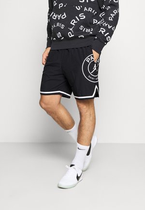 Pantalones cortos negros con acentos blancos, con un logo redondo y el texto "PARIS". Se llevan con una sudadera negra a juego y calcetines blancos con el logo negro.