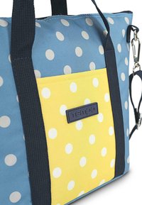 Bolsa de mano con lunares azules y amarillos, con asas negras resistentes, que cuenta con un bolsillo frontal amarillo y una superficie texturizada con un logo.