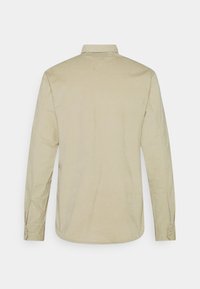 Camicia beige a maniche lunghe con polsini abbottonati, colletto classico e senza motivi visibili, mostrata di schiena su uno sfondo bianco.