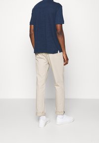 Námořnické tričko s krátkým rukávem a dvěma zadními kapsami, spárované se světlými kalhotami s ohrnutým lemem a bílými teniskami na světlém pozadí.