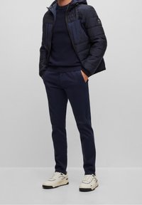 Námořnická zateplená bunda s kapucí, texturovanými panely, spárovaná s námořnickým svetrem a odpovídajícími kalhotami. Bílí tenisky dotvářejí vzhled.