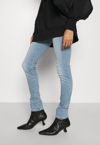 Jeans skinny de color azul claro combinados con botas de tobillo negras de punta afilada y tacón. Los jeans tienen una textura clásica de denim.