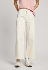 Pantaloni larghi di colore crema realizzati in cotone, con vita alta, chiusura a bottoni e orli arrotolati, abbinati a sneakers beige.
