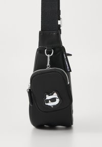 Černá krosna s přední zipovou kapsou, která má nášivku kočky s brýlemi a textilní štítek "Karl Lagerfeld" na boku.