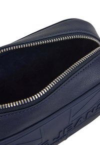Funda de cuero azul marino con cremallera plateada. Exterior texturizado y interior oscuro sólido. Presenta un logotipo en relieve en el lado.