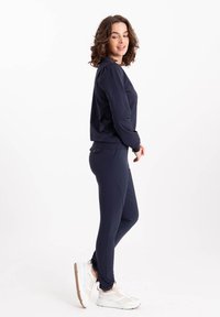 Marineblauwe pullover met lange mouwen, gecombineerd met een bijpassende fitted legging. Beide gemaakt van zachte, rekbare stof. Witte sneakers met beige accenten.