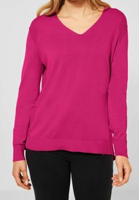 Svetr s V výstřihem v jasně růžové barvě, vyrobený z měkké pleteniny. Má dlouhé rukávy a žebrované detaily na manžetách a lemu.