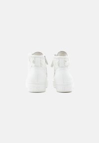 Ζευγάρι λευκά ψηλά αθλητικά παπούτσια με σχέδιο δαντέλας και φερμουάρ στα πλάγια, φαίνονται από πίσω πάνω σε απλό φόντο.