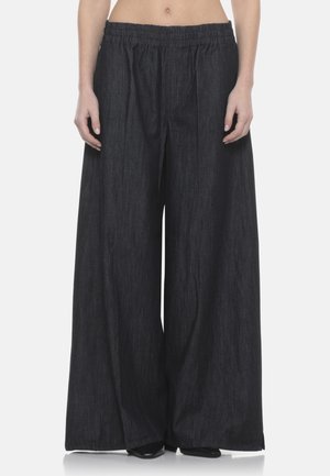 Pantaloni neri in denim a gamba larga con elastico in vita indossati da una persona in piedi su uno sfondo neutro.