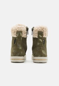 Botas de tobillo de ante verde oliva con puños de pelo sintético blanco, cremalleras laterales y patrones sutiles de hojas; suelas de goma con una base beige clara.