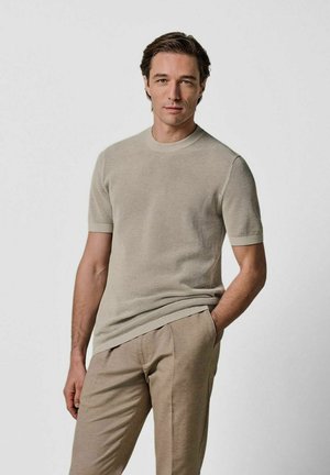 T-shirt a maniche corte color beige chiaro in maglia a coste con scollo rotondo. Abbinate a pantaloni sartoriali beige chiaro. Tessuto morbido e strutturato.
