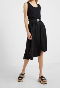 Top sin mangas negro combinado con una falda midi negra con botones. La falda cuenta con una cinturilla fruncida y fluye de manera suelta. Sandalias de plataforma negras.