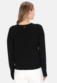 Black ribbed sweater featuring a round neckline, long sleeves, and a subtle metallic accent at the back. Rounded hemline and textured fabric.