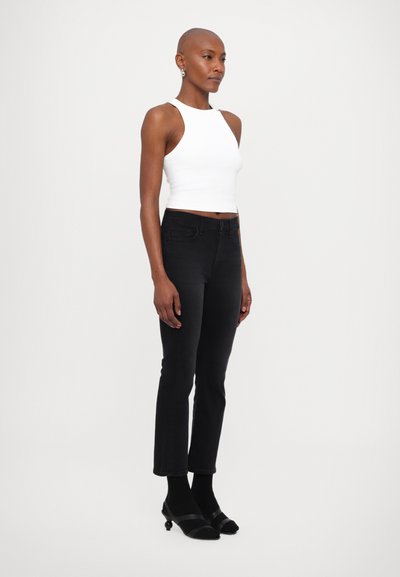 Jeans negri din denim cu o croială ajustată și tiv brut, asortați cu un top scurt alb ajustat. Look-ul este completat cu sandale negre, ușor de încălțat.