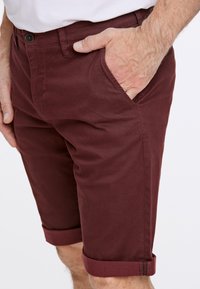 Maroon shorts med en texturerad mönster, med sidofickor och rullade fållar. Tillverkade av hållbart tyg med en tight passform.