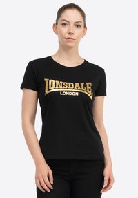 Melnā kokvilnas T-krekls ar īsām piedurknēm un apaļu apkakli. Priekšpusē ir zelta krāsas uzraksts "LONSDALE" un "LONDON".