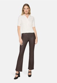 Polo blanc texturé avec col, associé à un pantalon évasé marron foncé et des chaussures à talons noires. Le mannequin est debout dans une pose neutre.