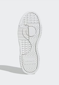 Suela de zapatilla blanca con patrones texturizados, incluyendo rayas onduladas y horizontales, con un logotipo en relieve en el área del talón.