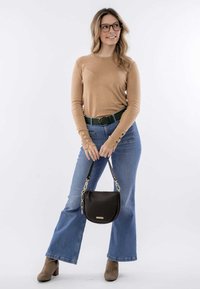 Tanshirt met lange mouwen en knoopdetails, groene riem, blauwe flared jeans, bruine handtas met gouden hardware en beige enkellaarsjes.