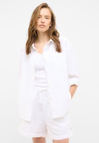 Biała lniana koszula z zapięciem na guziki, luźny krój, kieszeń na piersi, zestawiona z białymi lnianymi szortami z elastycznym pasem i sznurkiem.