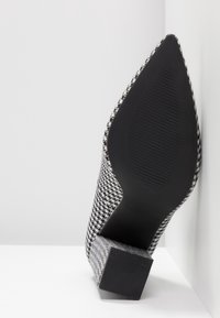 Chaussure à bout pointu en motif pied-de-poule texturé noir et blanc, avec un talon noir épais et une semelle en caoutchouc nervurée.