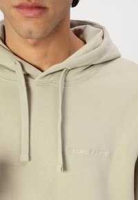 Mikina s kapucňou z mäkkej, svetlozelenej tkaniny s predným klokankovým vreckom a vyšívaným logom "LYLE & SCOTT" v svetloružovej farbe.