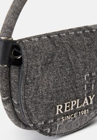 Borsa a tracolla in denim grigio con forma curva, dettagli in pelle nera e logo dorato "REPLAY SINCE 1981" sul fronte. Superficie texturizzata.