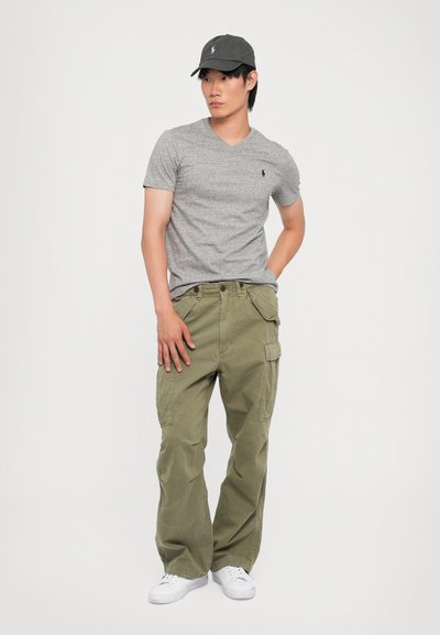 Γκρι μπλούζα v-neck, ελαιόχρωμο cargo παντελόνι, λευκά sneakers και σκούρο γκρι καπέλο; άνετη εφαρμογή, ορατό λογότυπο στη μπλούζα και το καπέλο, πολλαπλές τσέπες στο παντελόνι.