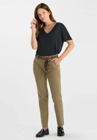 T-shirt noir à col en V associé à un pantalon-tailleur vert olive avec une ceinture à imprimé léopard et des mocassins noirs. Textures de tissu lisses, design ajusté.