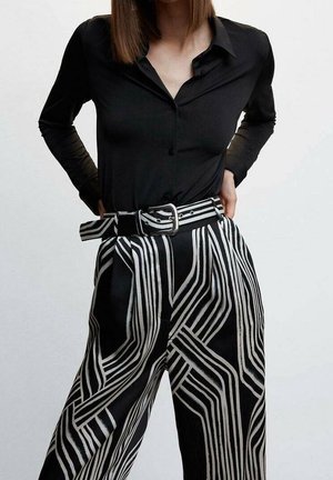 Une chemise noire à manches longues associée à un pantalon taille haute avec de grandes rayures abstraites blanches. L'ensemble comprend un détail de taille ceinturée.