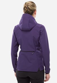 Femme aux cheveux tressés portant une veste à capuche violette, vue de dos, avec une poche zippée près de la taille.