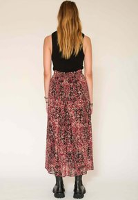 Jupe maxi à imprimé floral avec des nuances de rose et de noir, dotée d'une taille froncée et d'un tissu léger. Associée à un haut sans manches noir.