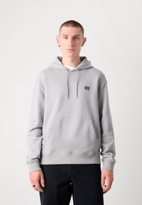 Grijze hoodie met een kangoeroezak, trekkoordcapuchon en een klein logo label. De stof lijkt zacht en gestructureerd, met ribgebreide manchetten.