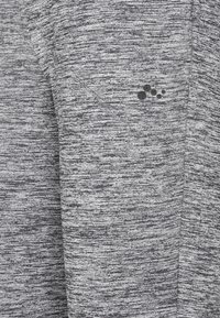 Grå atletisk tyg med ett texturerat mönster, med en liten svart logotyp av prickar. Materialet verkar mjukt och elastiskt, vilket gör det idealiskt för träningskläder.