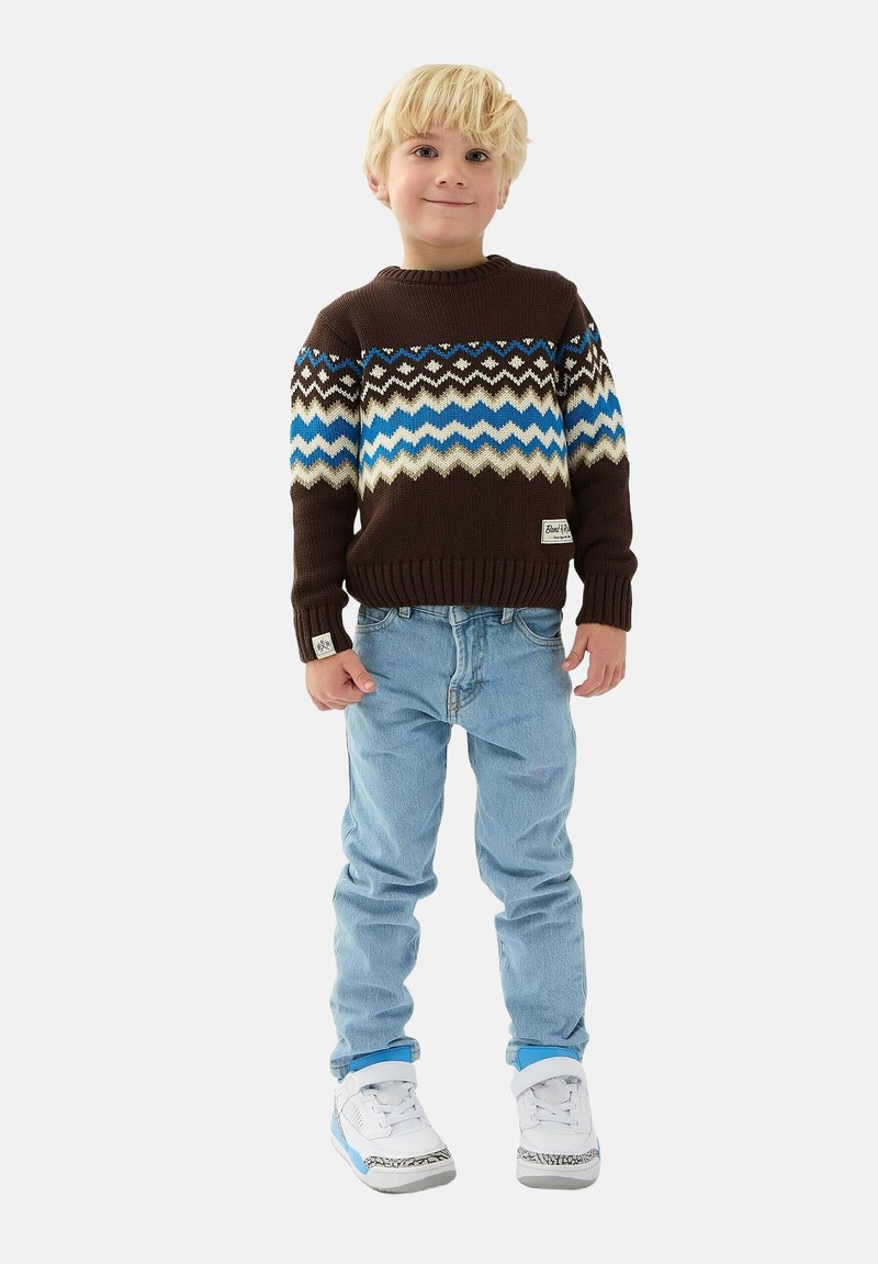 Brun stickad tröja med ett blått och krämfärgat zigzagmönster, ihopparad med ljusblå jeans och vita sneakers med blå detaljer.
